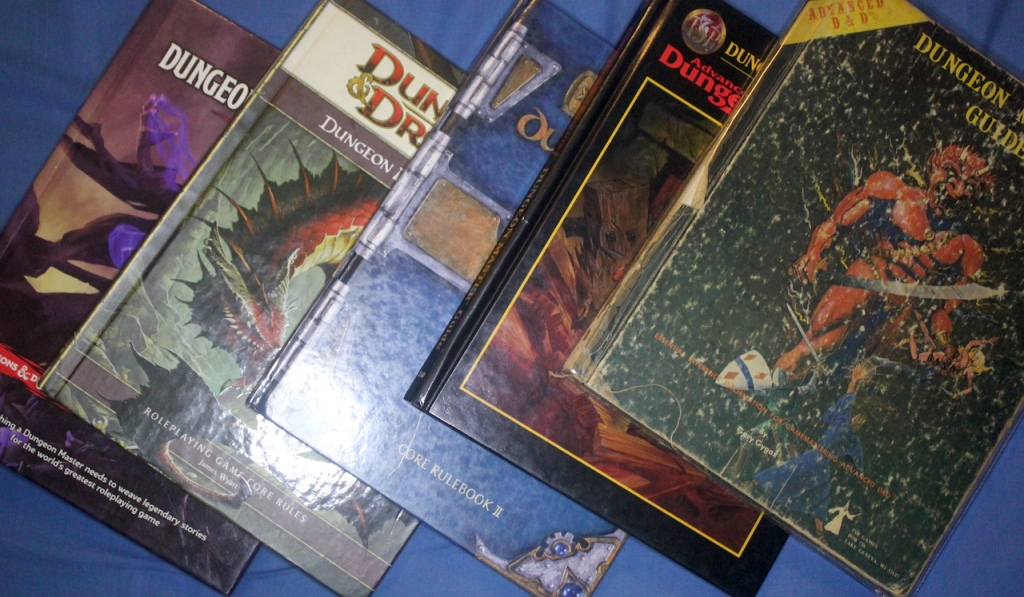 left to right. The Dungeon Master's guides for fifth edition Dungeons and Dragons, fourth edition, third edition, second edition revised, and first edition.
